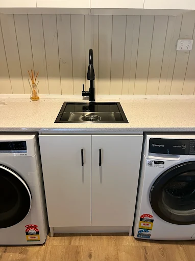 Laundry sink with black tap and cabinet between washing machines